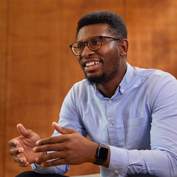 Chidi sedí, usmívá se a dívá se mimo objektiv.