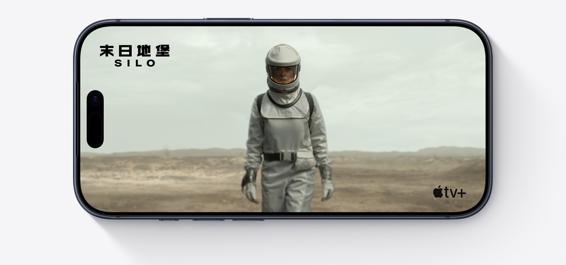 橫放的 iPhone，機身正面，螢幕顯示 Apple TV 劇集《末日地堡》(Silo) 的劇照，角色身穿太空衣