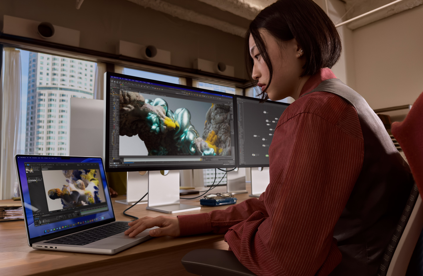 Asmuo, sėdintis ofisą primenančioje aplinkoje, dirba su „MacBook“ nešiojamuoju kompiuteriu, kuris yra prijungtas prie „Studio Display XDR“ naudojant „Thunderbolt 5“ prievadą