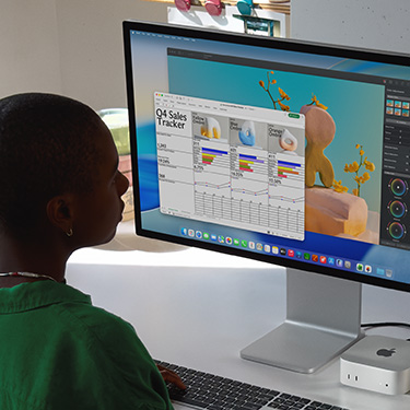 Employee sits and works on an Excel spreadsheet titled 'Q4 Sales Tracker' on iMac and Mac Mini. Behind the Excel spreadsheet is a Pixelmator Pro window and the macOS Tahoe background.
