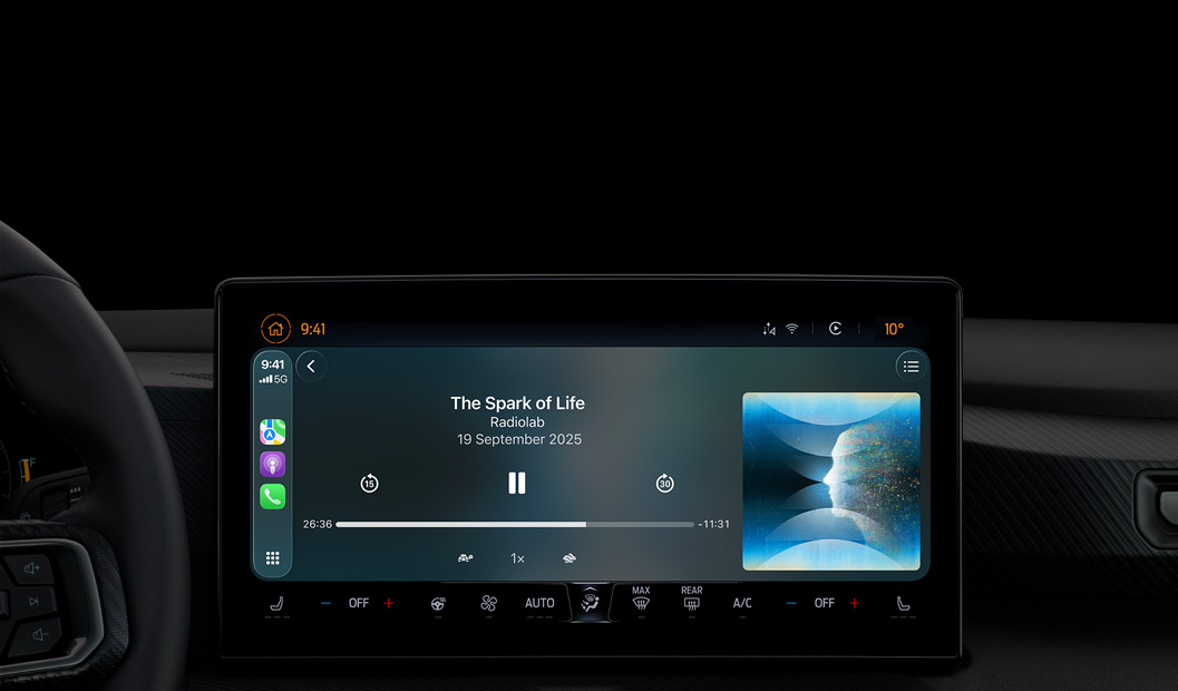 A car interior, centre console display shows Apple&nbsp;Podcasts playing via CarPlay, now playing “The Spark of Life” podcast by Radiolab, playback controls include skip back, pause and skip forward.