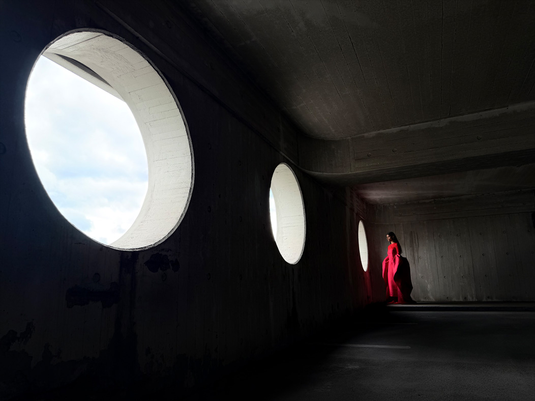 Femme portant une longue robe rouge photographiée dans une pièce vide. L’app Photos montre les distances focales pour illustrer les capacités du système caméra Pro : 24 mm